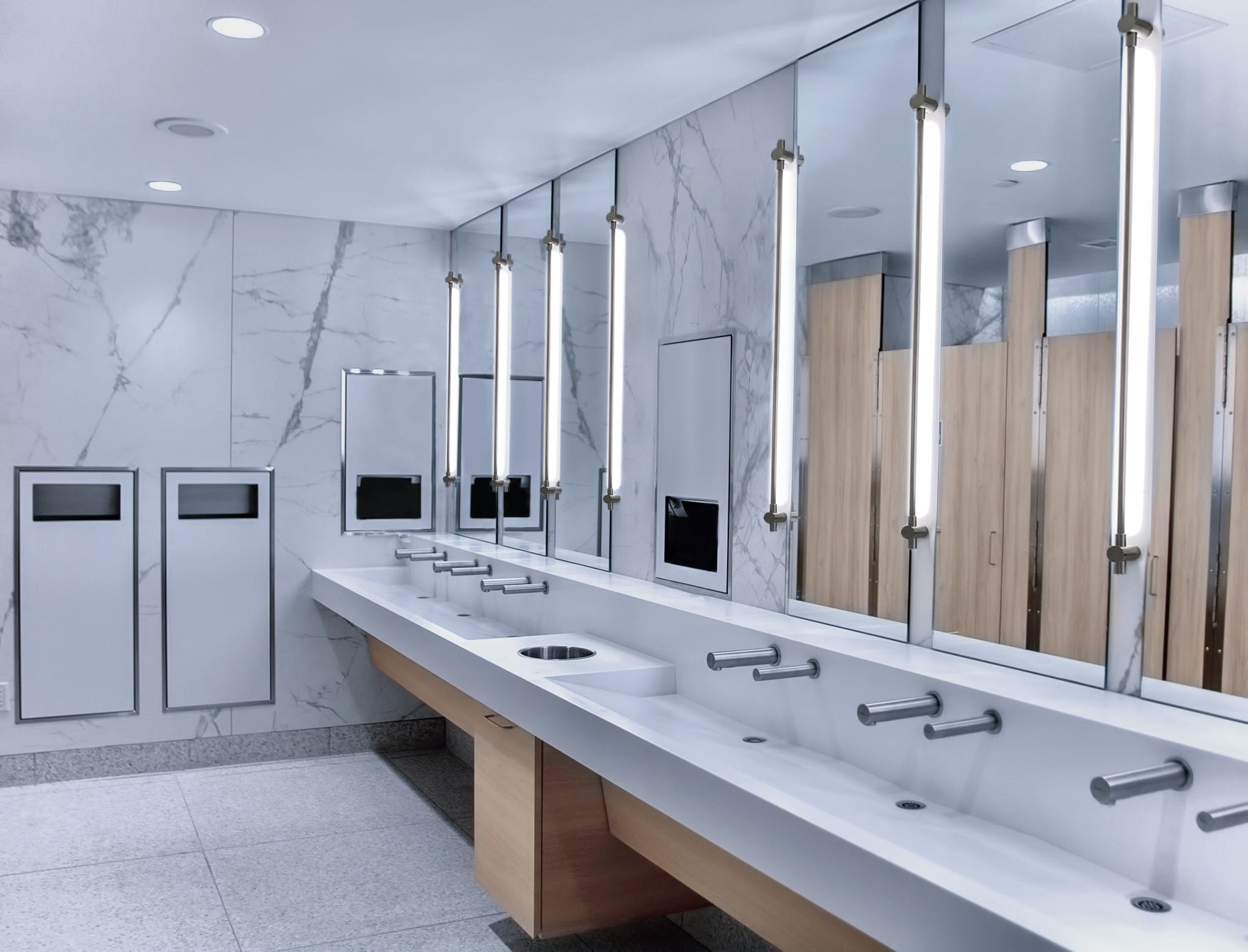 AquaGUARD solid surface trough sink module with trash cutout in commercial restroom.